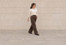 Woman with a low ponytail walking in an ivory jumper, chocolate wide-leg trousers and brown loafers.