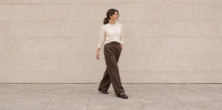 Woman with a low ponytail walking in an ivory jumper, chocolate wide-leg trousers and brown loafers.